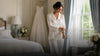 Bride wearing elegant button-up pajamas in a bright bridal suite with her wedding dress in the background